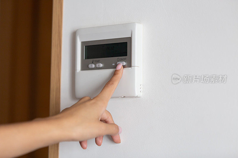 一个年轻女子的手按下空调或加热器的开/关按钮的特写